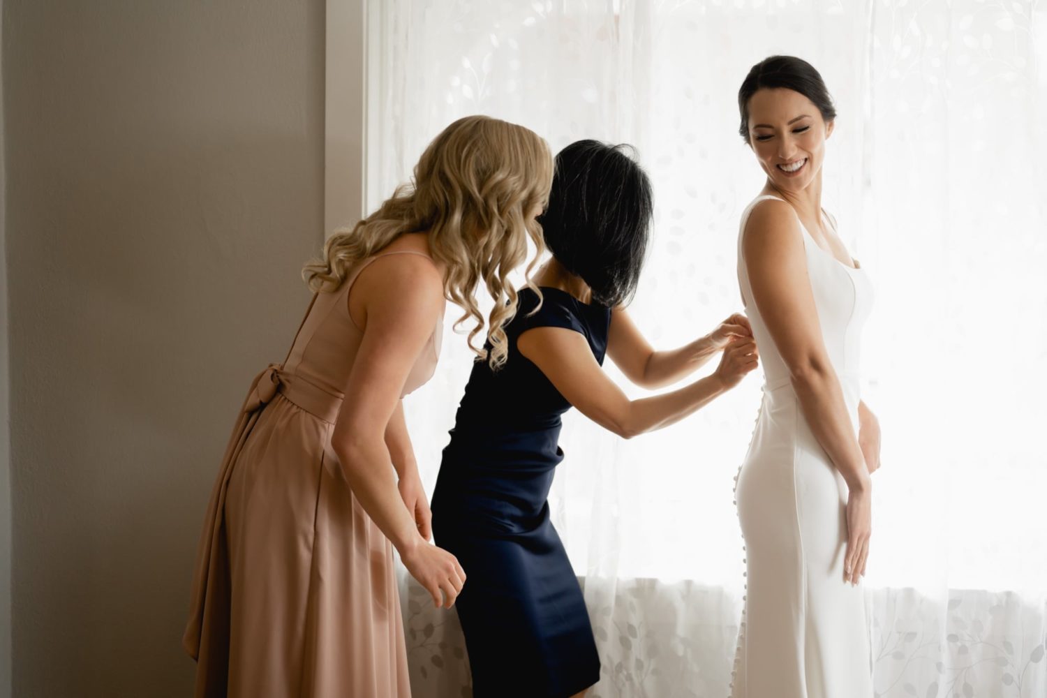Mother of the bride and maid of honor helping bride into wedding dress in Airbnb