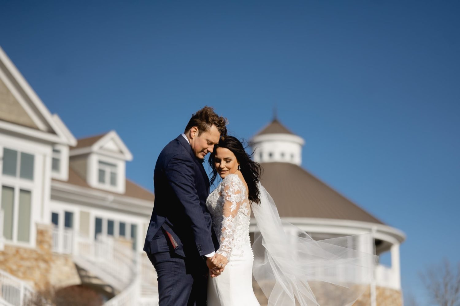 Bride and groom cuddling on a chilly spring day in front of Glen Oaks country club