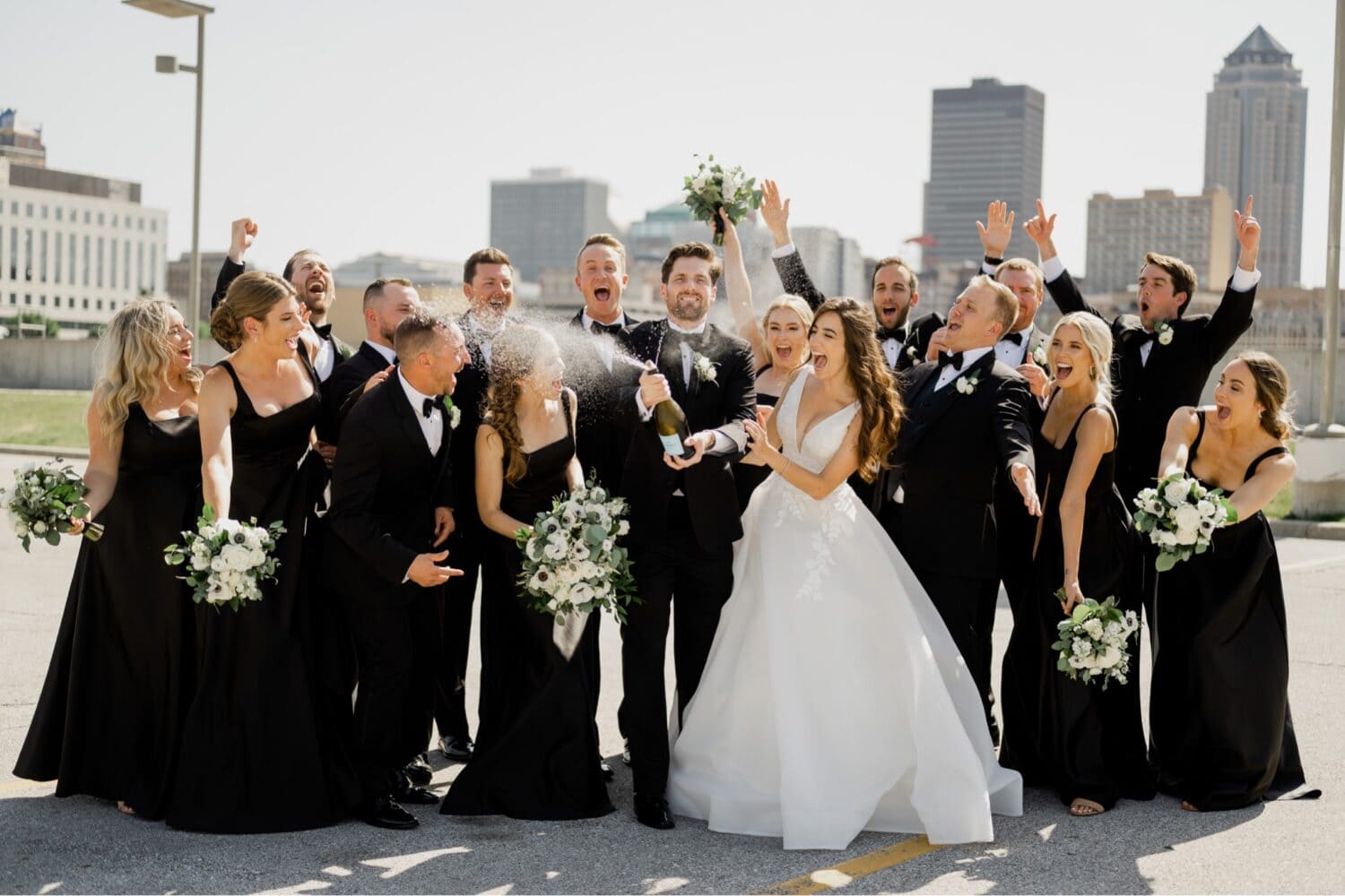 wedding party spraying champagne in front of the des moines skyline