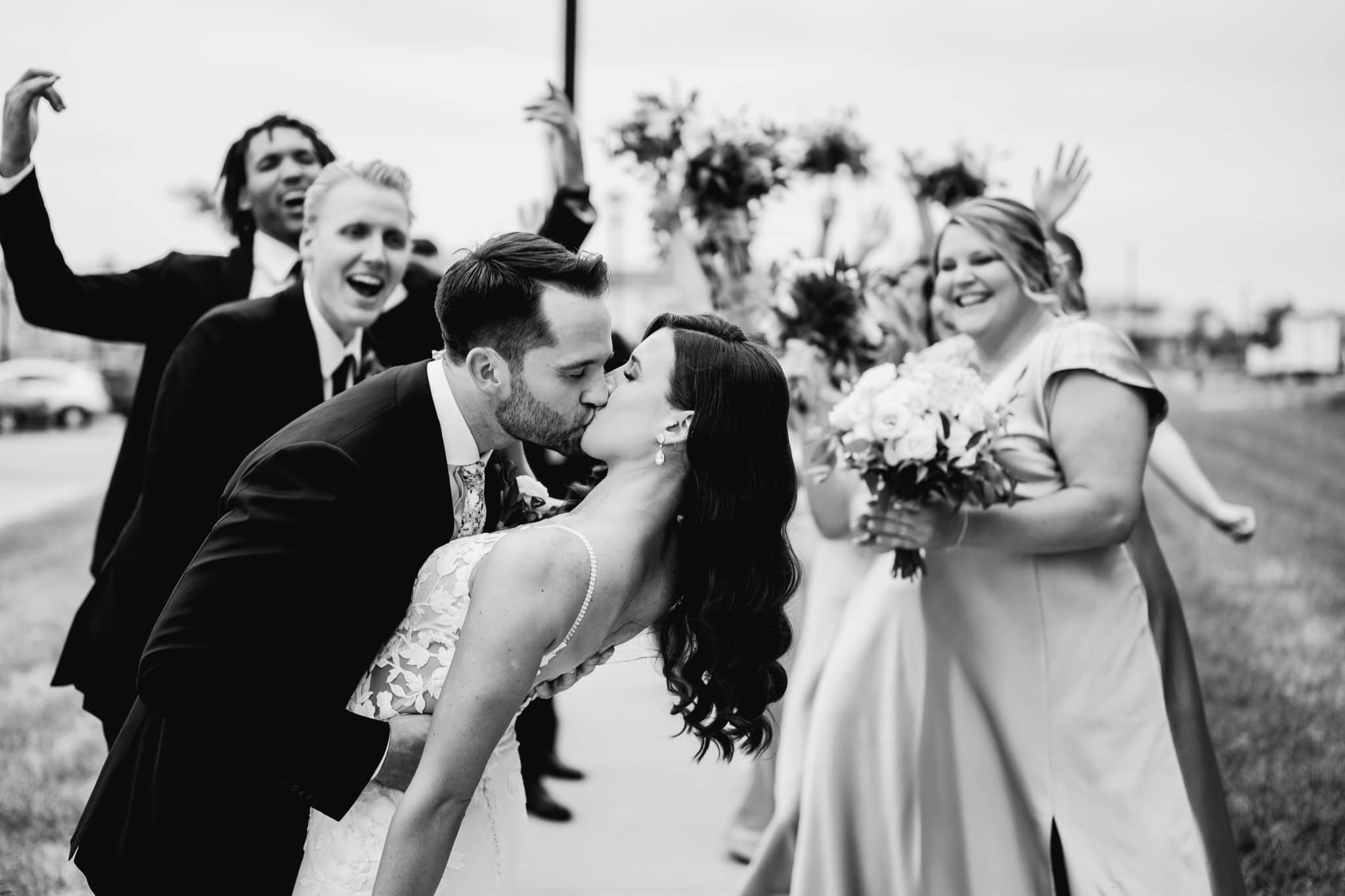 bride and groom dip kiss with wedding party