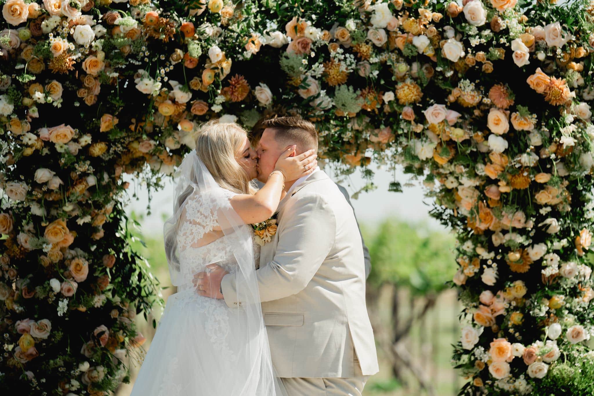 bride and groom kiss in front of beautiful floral arch